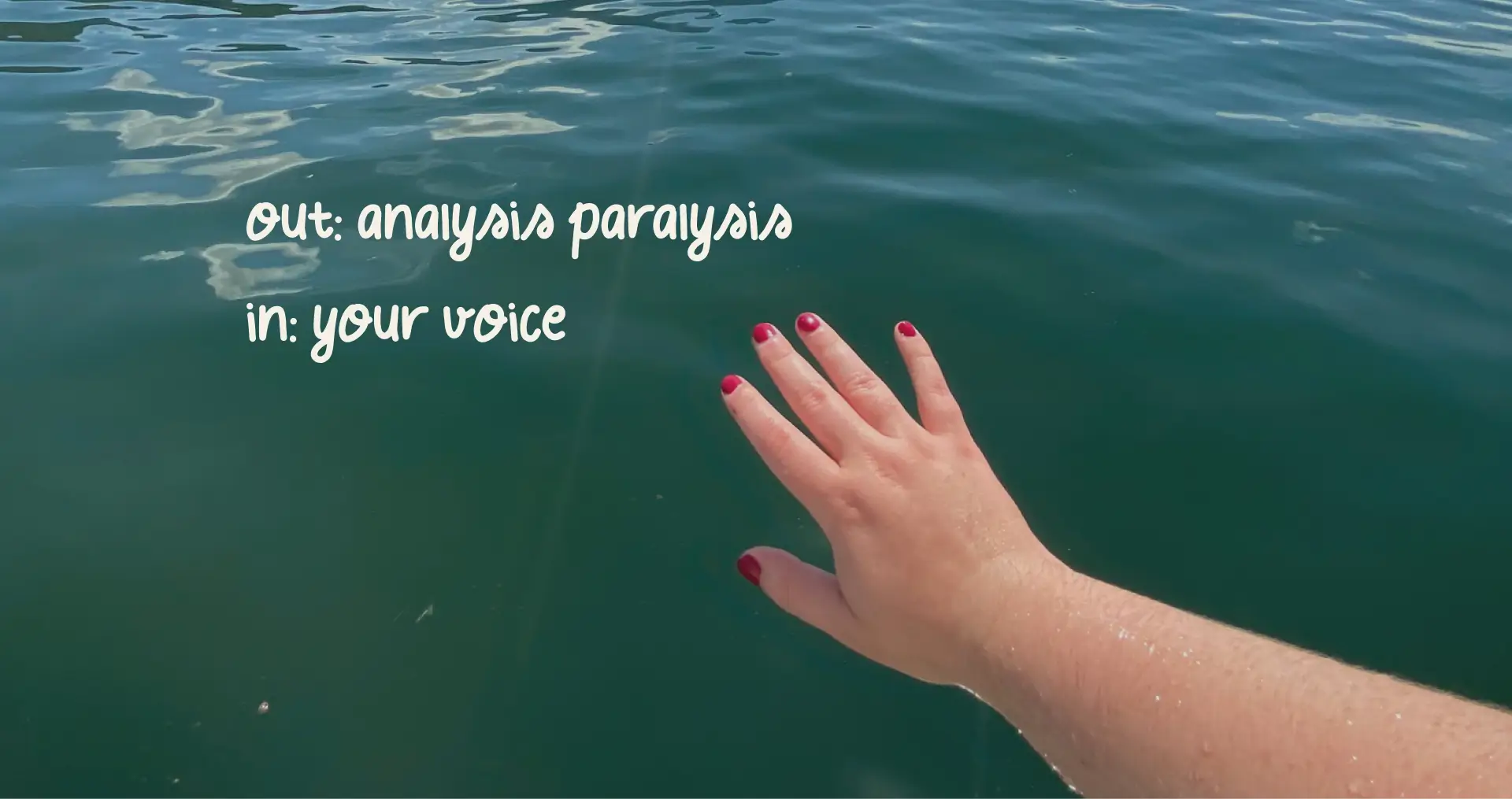 Mariia's hand, nails painted in berry red, against the lake.